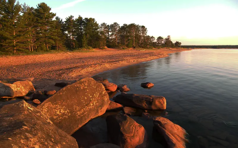 Sunrise illuminates a long beach near calm water.