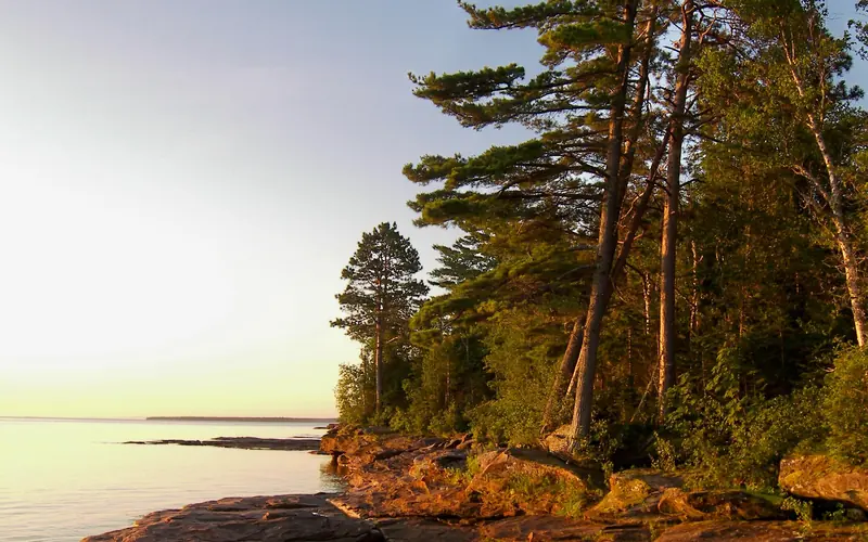 A rocky shoreline meets the calm water of a lake at sunset.