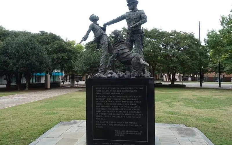 Statue of a boy being grabbed by a policemen who is holding a dog posed to bite on a leash