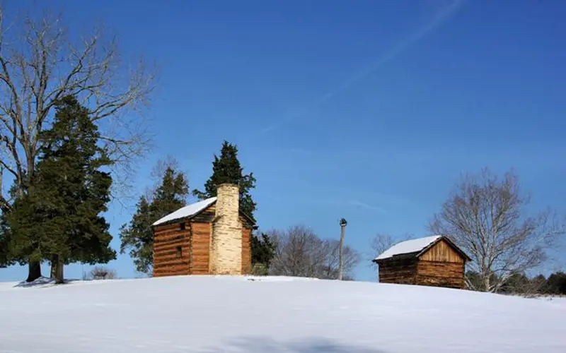 Back side of kitchen cabin and smokehouse in snow with blue sky and trees