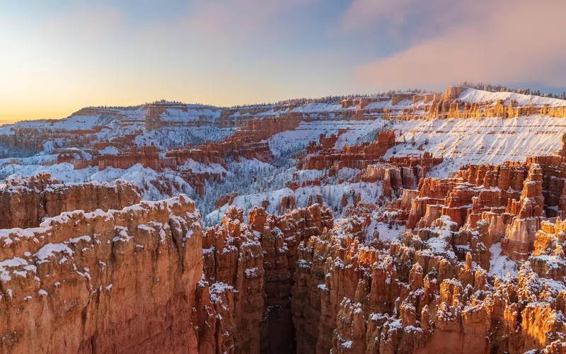Snow blankets a red rock landscape of tall rock spires beneath an early morning sky