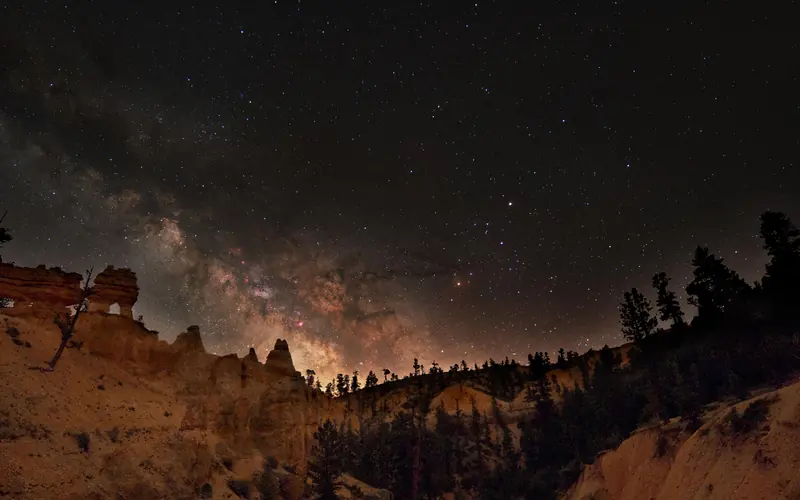 The center of the Milky Way galaxy is seen rising above a horizon of forest and red rock spires