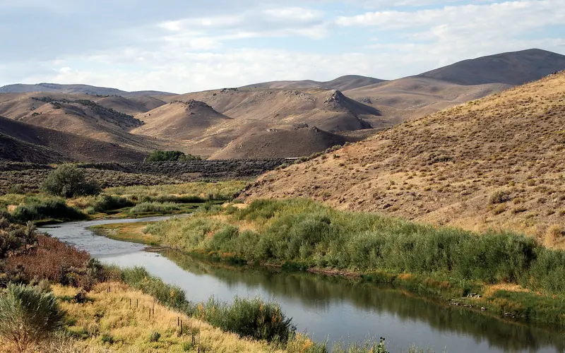 A still creek winds through brown rolling hills.