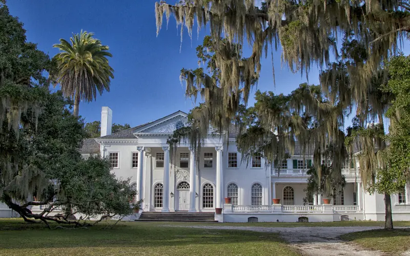 large, white mansion behind oak trees draped with Spanish Moss