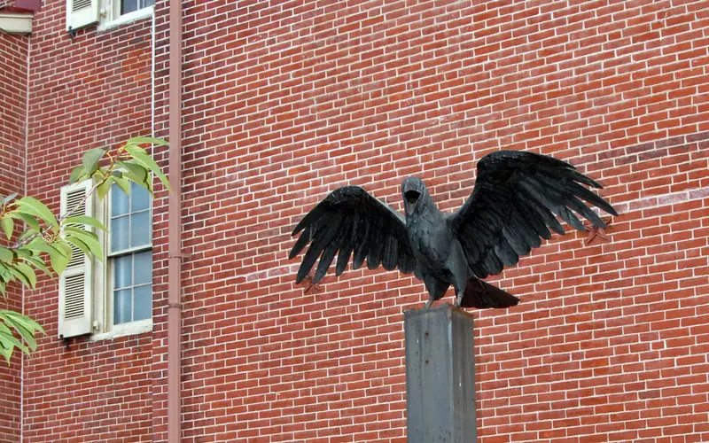 Color photo showing a large raven statue with wings outspread on a metal plinth.
