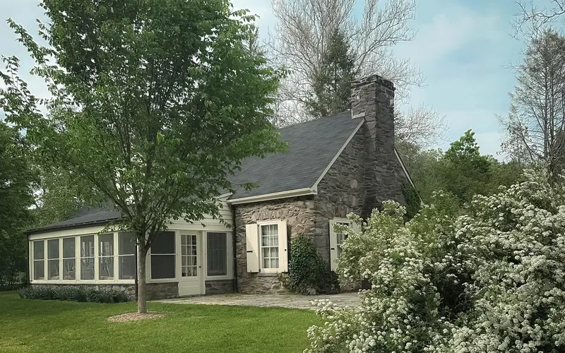 A small fieldstone cottage on a lush lawn with flowering shrubs.