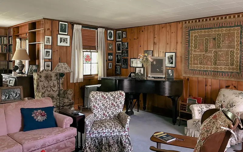 A paneled room with comfortable furniture and a baby grand piano.