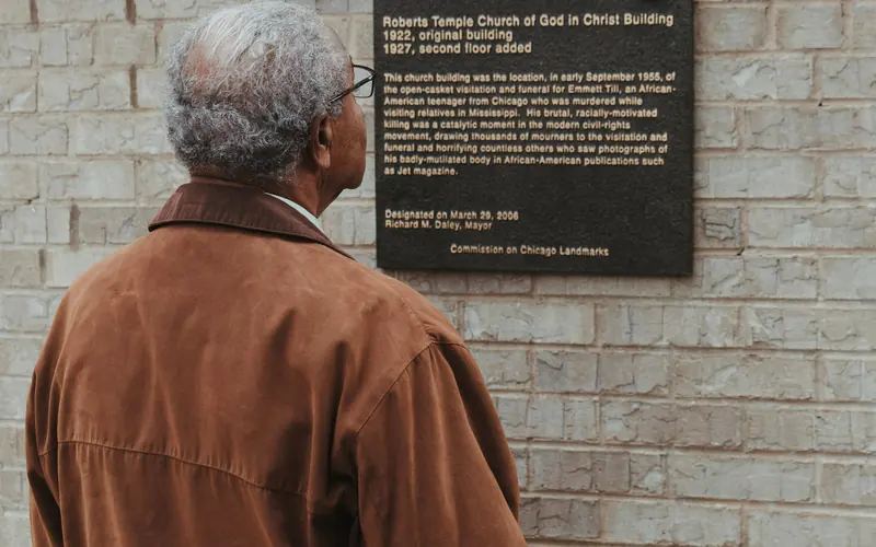 An elderly African American man looks at a plaque on the church exterior.