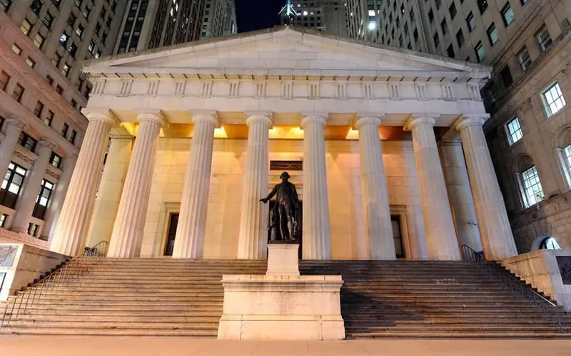A stone, Grecian-style building, with columns and a statue in the front.