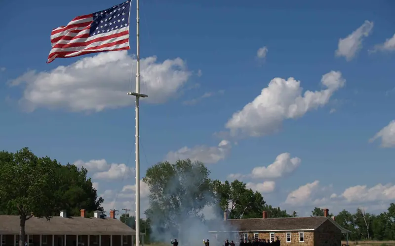 Men in 19th century U.S. Army uniforms lower an American flag.