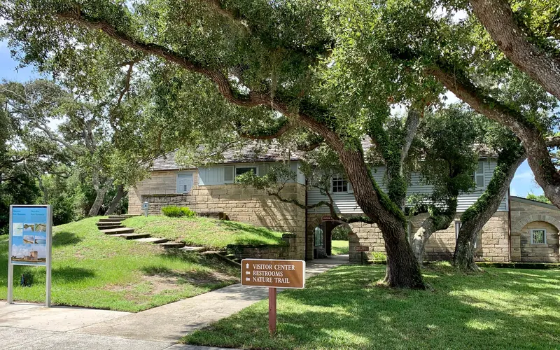 Two story building with stone base and wood second floor, oak trees, grass, two signs.