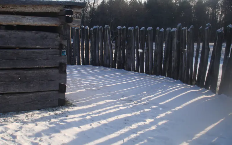 cabin and stockade casting shadows on the snow