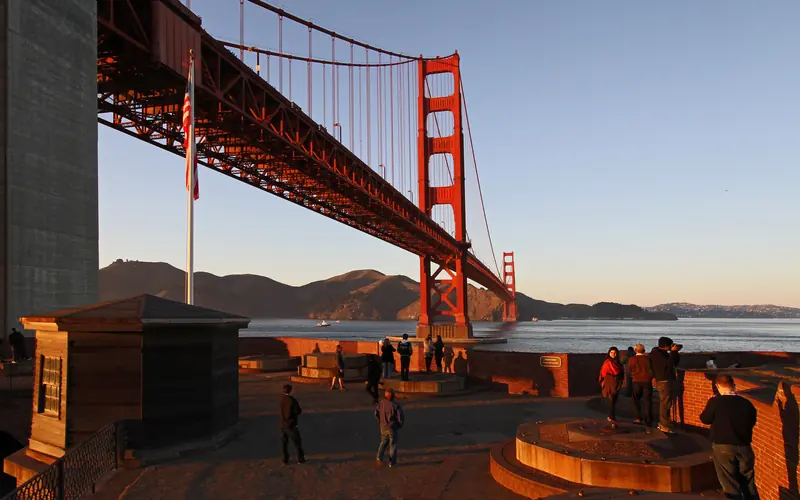 Golden sunset light on the roof of Fort Point with Golden Gate Bridge and bay behind.