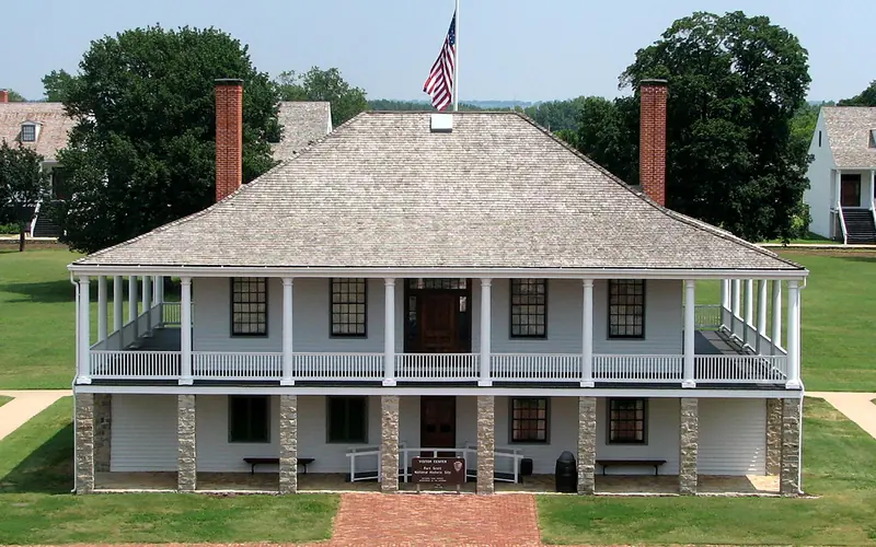Picture of the post hospital with the parade ground and trees in the background.