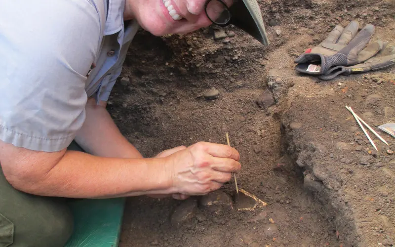 A woman digs in a carefully excavated hole.