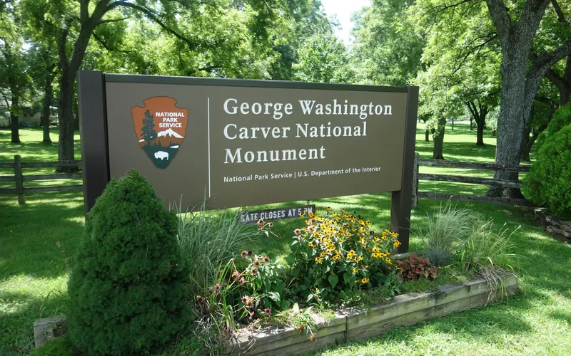 An entrance sign to George Washington Carver National Monument with wildflower and plants.
