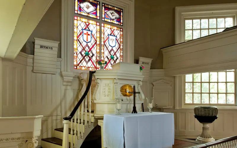 A color photo of the interior of Gloria Dei Church showing the pulpit and a stained glass window.