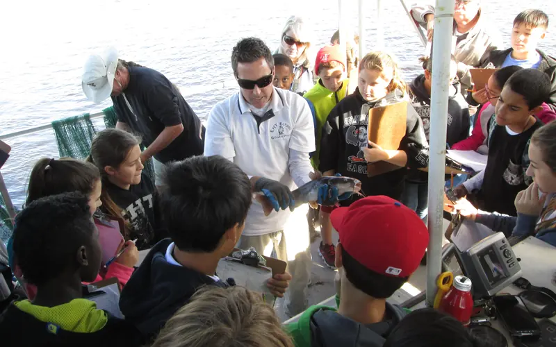 School group examines a fish held by the instructor.