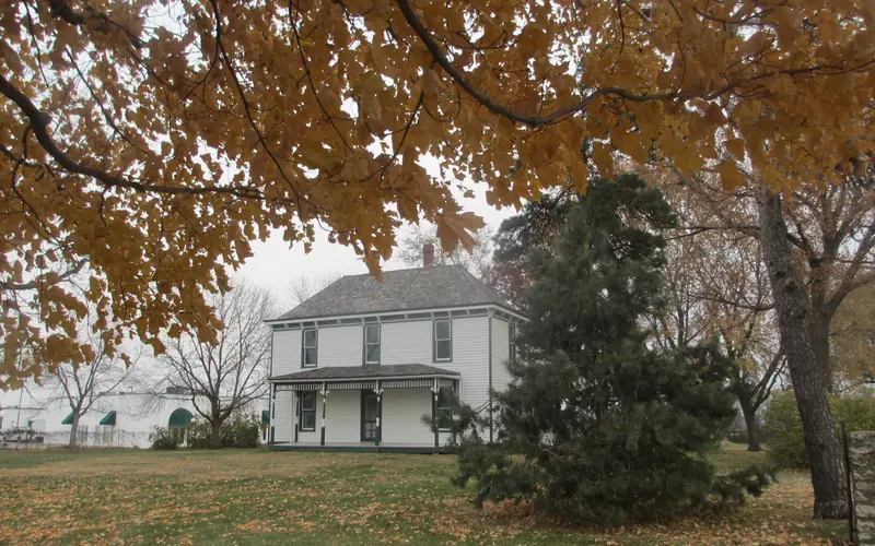 The Truman Farm Home sits behind Autumn trees.