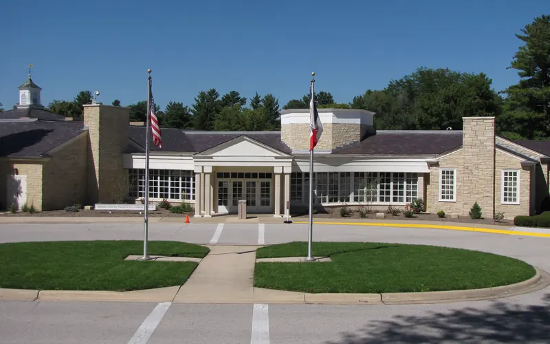 A sprawling one story public building of rough-faced yellowish stone has a white portico entrance.