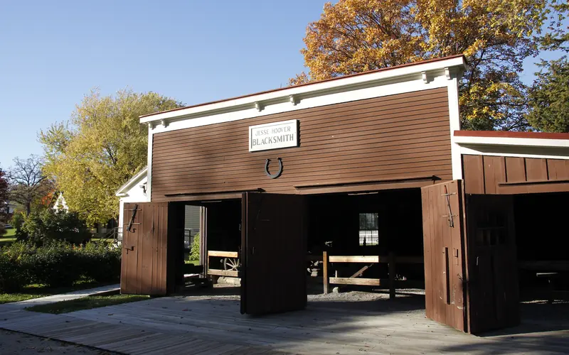 A low brown barn-like building with three large doorways has a large horseshoe on its facade.