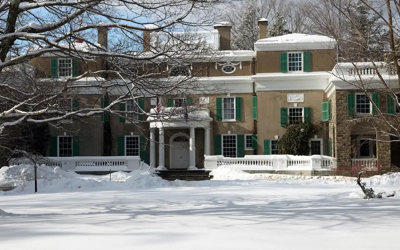A stucco house with wood portico surrounded by a snowy lawn.