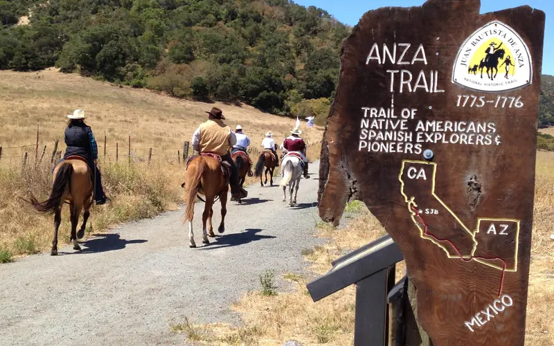 equestrians walk down a dirt trail with an Anza Trail marker