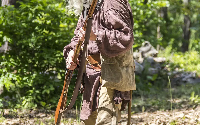A patriot rifleman stands ready to fire his weapon.