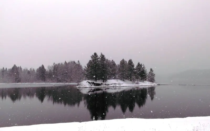 Snow falls over a small peninsula with its clear reflection over the waters.