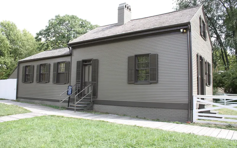 1 story small gray house with stairs leading up to door.