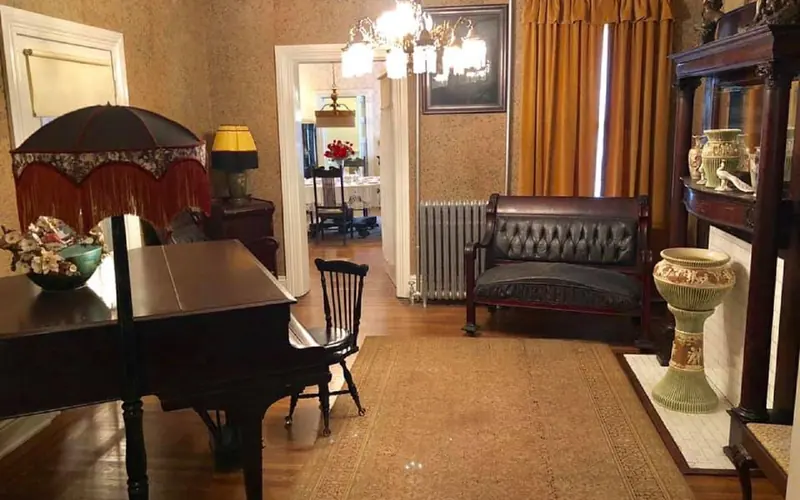 The back parlor with piano, couch, floor lamp and fireplace