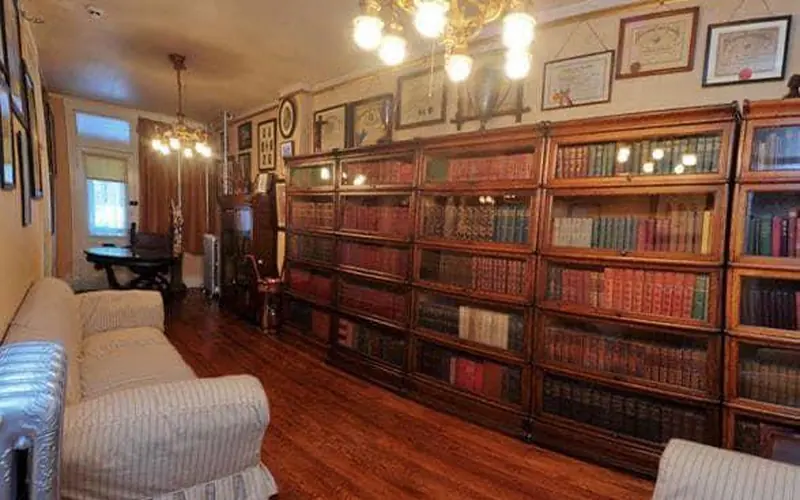 A room with a wall of full bookcases, chairs and several diplomas on the wall