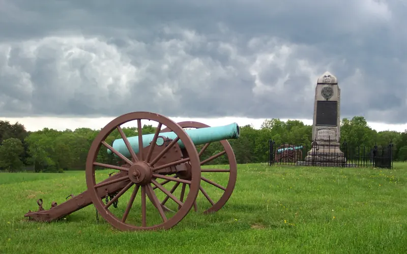 Civil War cannon and granite and bronze monument under a cloudy sky.