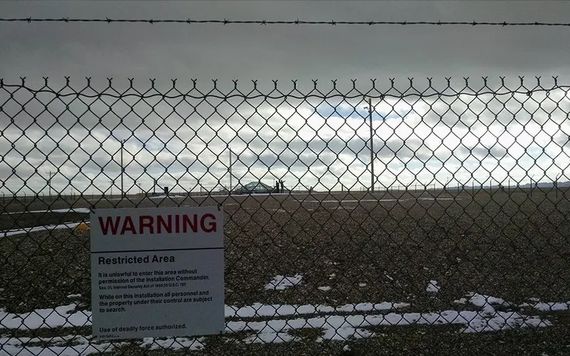 Two people are visible at the missile silo through a chain link fence