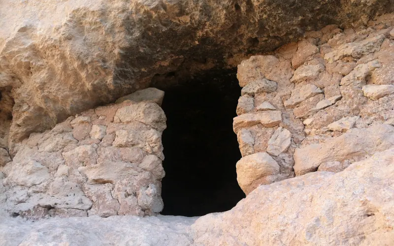 Two masonry walls with a dark doorway in a short cliff ledge.