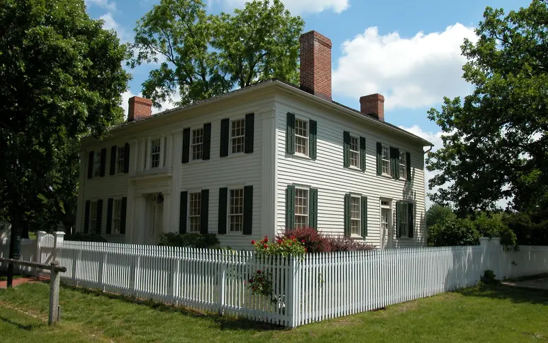 A large, white, two-story historic wood home with a red roof and white picket fence.