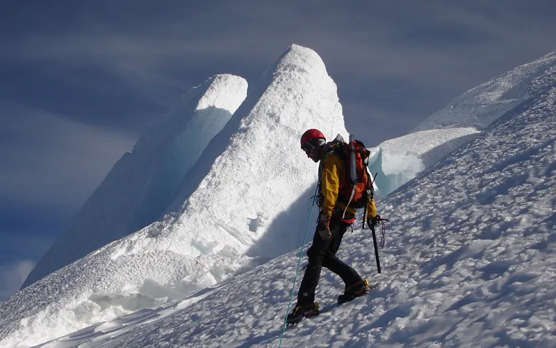 Climber on glacier steps downward with icy crags in background.