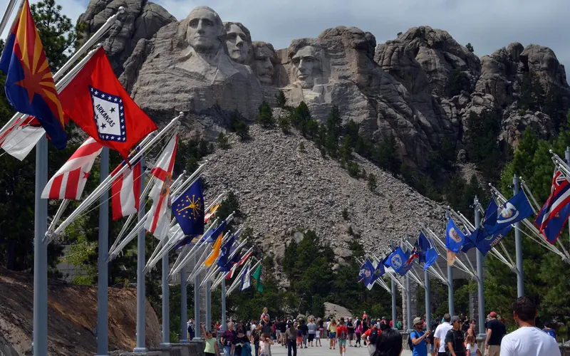 Visitors walking along the Avenue of Flags with Mount Rushmore in the background.