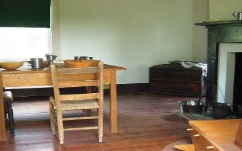 Room containing very simple wood table and chair, and baby cradle with fireplace in background