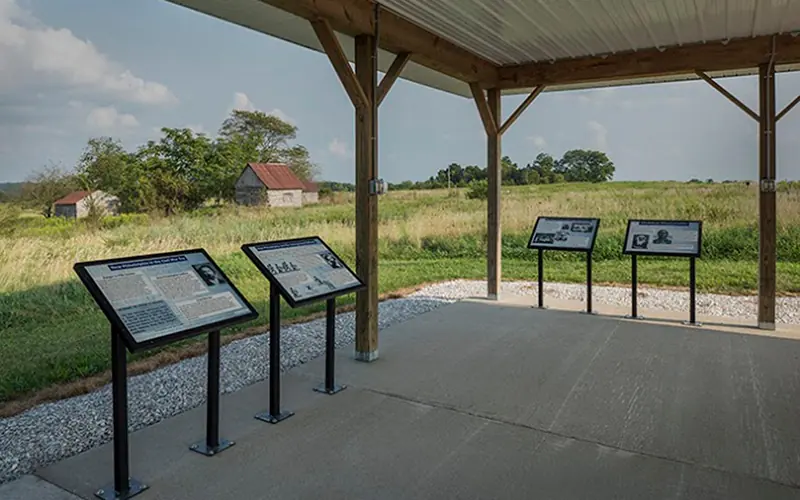 Four interpretive panels mounted under a covered, open-sided kiosk overlooking a prairie landscape.