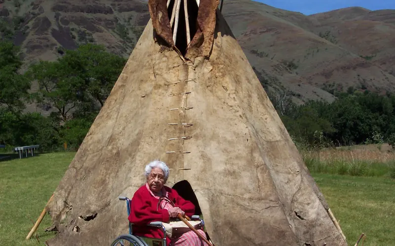 Elder (Mylie Lawyer) sitting in front of Old Buffalo hide tipi.