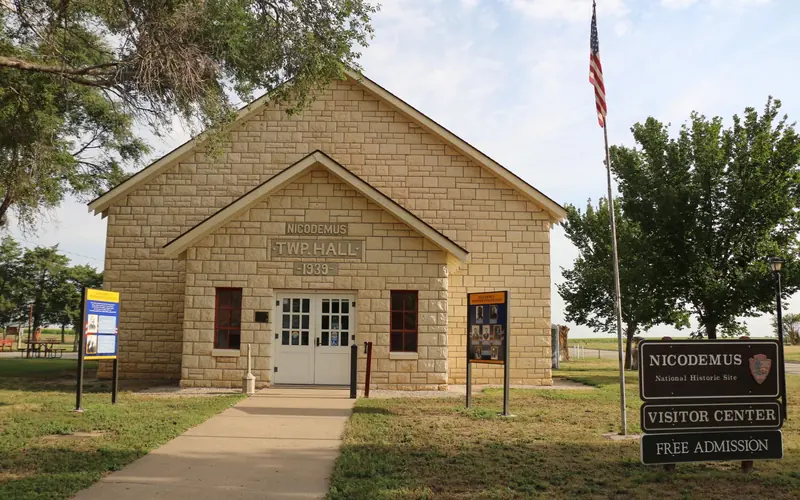 Front view of limestone building. A sidewalk leads up to white double doors of the building.
