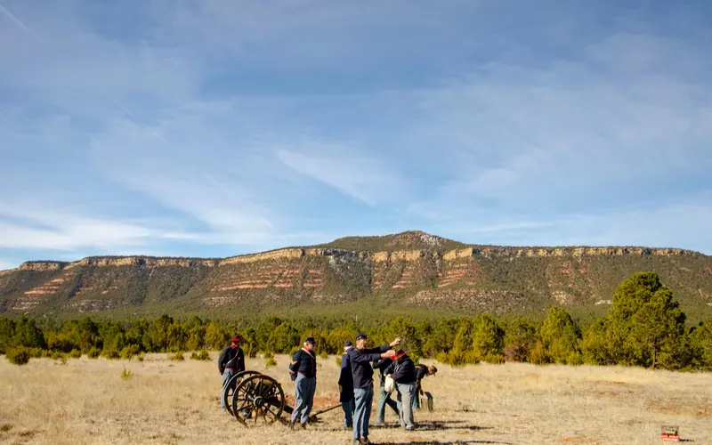 Reenactors prepare a cannon under a mesa and blue skies.