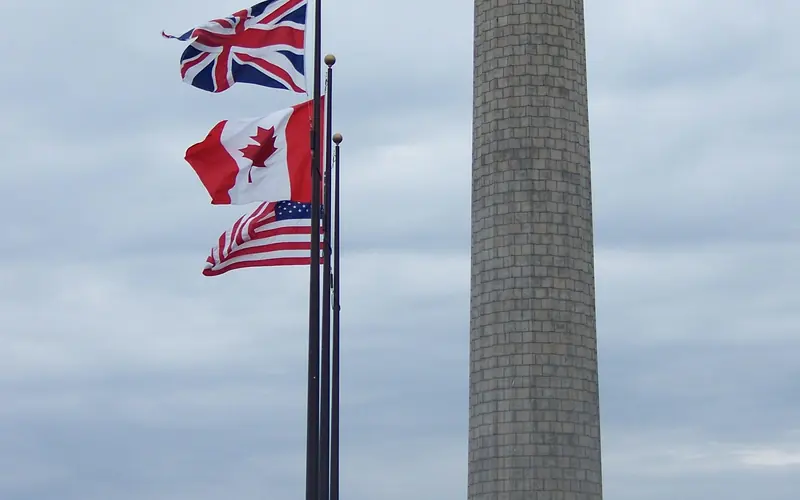 The Memorial Column with the United Kingdom, Canadian, and US Flags flying from poles on the lawn.