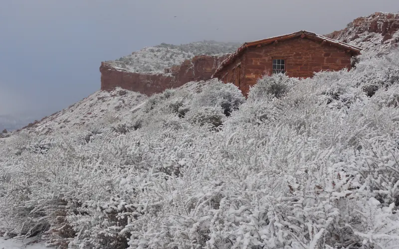 A red-orange sandstone cabin surrounded by white snow.