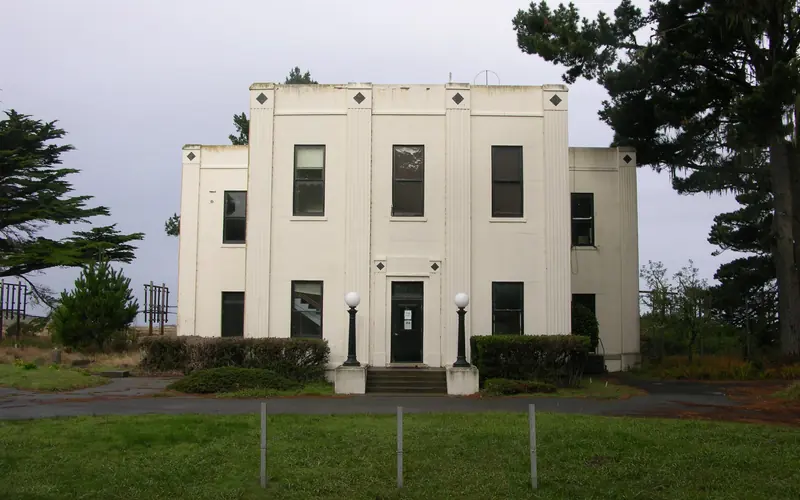 A white, two-story art deco building beyond a green, grassy round-about.