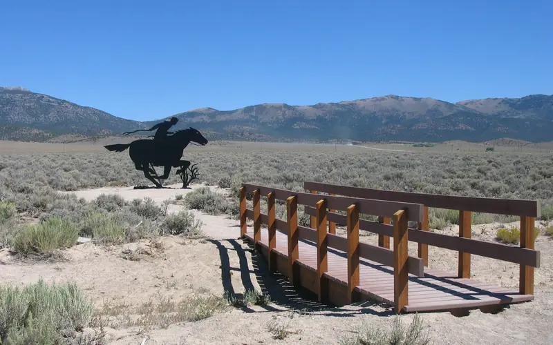 A footbridge leads to a dark steel silhouette of a Pony Express rider.
