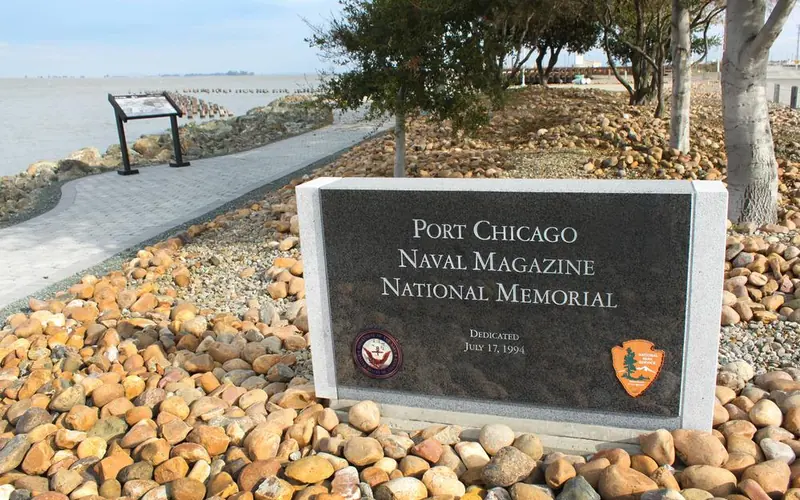 Park signs sitting in rock bed. Trees and bay in background.