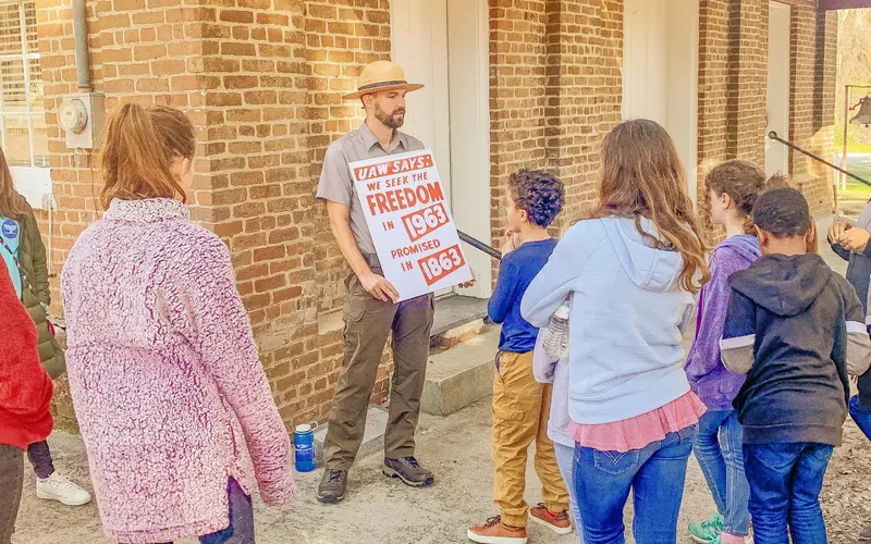 A park ranger holds a sign while talking to young people.