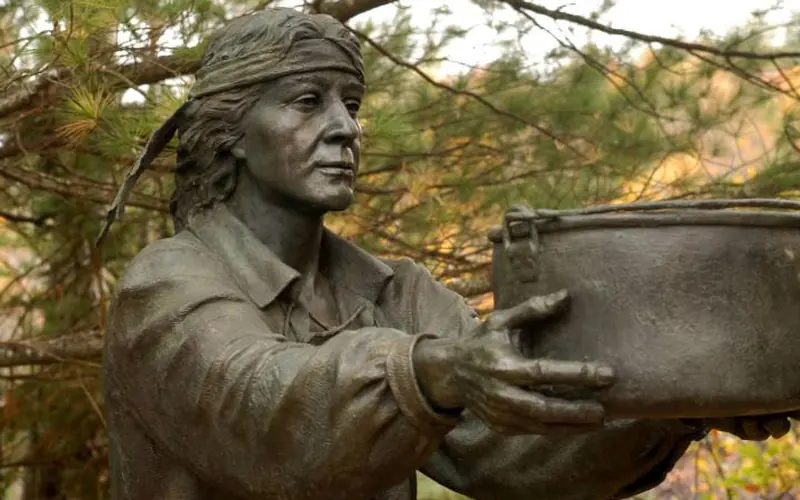 A bronze sculpture of a Passamaquoddy person reaching out to assist the French settlers.